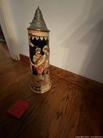 Front view of ceramic stein with relief figures and pewter lid