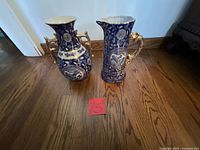 Both blue and white ceramic vases with gold-tone handles on wooden floor