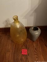 Yellow glass vase alongside gray vase on hardwood floor