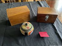 Two wooden boxes and one painted container displayed on black cloth