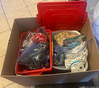 Cardboard box with red LEGO bin and white laundry basket filled with bagged LEGO pieces