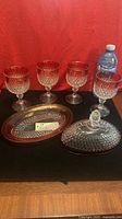 Four ruby flashed Diamond Point goblets, oval butter dish base and domed lid displayed on black surface