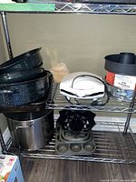 Overall lot view on wire shelving showing roasting pans, stock pot, sandwich maker, cake and muffin pans, and doughnut kit