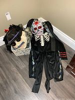 Lot overview showing skeleton costume, sugar skull mask, latex character mask in basket, hat