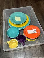 Plastic bin containing assorted multicolour Fiesta Ware bowls, plates and mugs