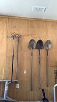 Three shovels and cultivator/hoe hanging on wall