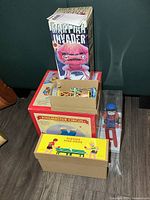 Stacked boxed tin toys showing Martian Invader, Ringmaster Circus, Playing Ping-Pong, brown plain boxes and skier figure