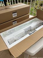 Open box showing packaged light fixture with frosted glass panel and two unopened boxes beneath