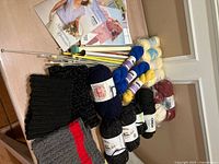 Overview of yarn skeins, knitting needles, pattern booklets and neck warmers