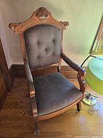 Full view of carved wooden armchair showing upholstery, arm pads, casters