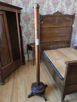 Full view of coat rack showing wood column, base, hooks, and brass crown top