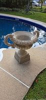 Full view of urn on pedestal beside pool showing overall form and proportions.