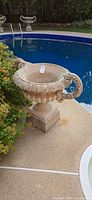 Front view of concrete urn on pedestal beside pool