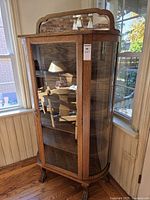 Full view of oak and glass curio cabinet showing curved glass front, shelves, and overall design