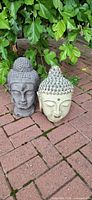 Both Buddha head statues side by side on brick surface