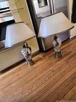 Two ceramic peacock motif table lamps with shades shown together on hardwood floor