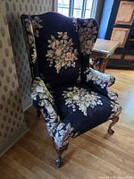 Full view of wingback armchair showing floral upholstery and carved legs