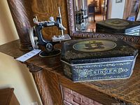 Singer toy sewing machine beside ornate Singer tin