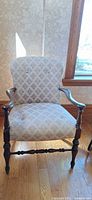 Front view of upholstered wooden armchair showing damask fabric, button-tufting, turned legs, wooden arms
