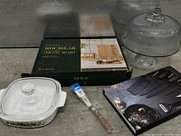 Group shot of boxed cheese board set, boxed knife set, glass cake stand with dome, CorningWare casserole