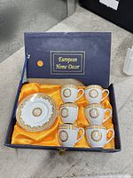 Box open showing six cups, one saucer, satin lining