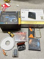Group shot showing boxed router, boxed CPU cooler, DeWalt device, earbuds, CDs, phone case, Ethernet cable, plastic storage case