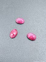 Three oval faceted rubies on dark background showing pinkish hue