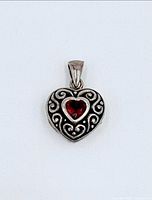 Front view of sterling silver heart locket with scrollwork and red garnet