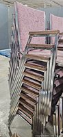 Stack of mauve fabric armchairs showing chrome frame and wood armrests
