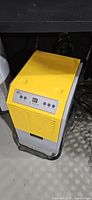 Front angled view of dehumidifier showing yellow top, control panel, grey body and base frame