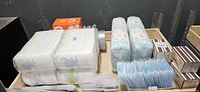 Overhead view showing stacks of diapers, two wrapped diaper bundles, blue disposable face masks, orange box of matches
