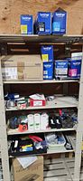 Full shelving unit showing Brother TN-227 toner cartridges, postal scale, tape dispensers, stapler, tape rolls and assorted office items