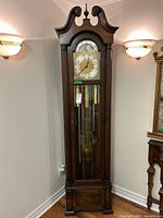Front view showing full height wood grandfather clock, glass door, brass face, weights and pendulum