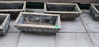 Four similar rectangular concrete planters visible, focusing on two central units with scroll design
