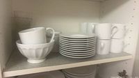 Shelf with white coffee mugs, fluted bowl, stacked saucers, pressed-glass tumblers