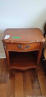 Full view of wood nightstand front showing drawer, handle, open shelf, carved details