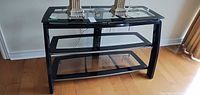 Front view of black metal and glass TV console showing three glass shelves