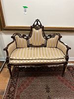 Front view of striped upholstered settee with carved wood frame