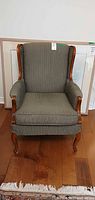 Front view of upholstered wingback armchair showing fabric, wood trim, legs
