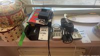 Overview of all items on windowsill: cameras, binoculars, chargers, packaging