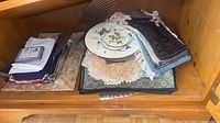 Overview of stacked linens, placemats, cork pieces and doilies inside cabinet