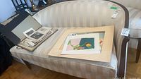 Sofa with black portfolio, loose prints, and two abstract paintings