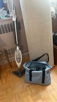 Full view of Shark steam mop standing upright beside blue accessory bag