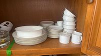 Stacks of plates, bowls, cups, creamer and sugar bowl on cabinet shelf