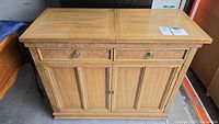 Front view of light oak sideboard with drawers and paneled doors closed, key visible in lock