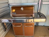 Front view of Weber Genesis grill showing overall design, cabinet, and hose