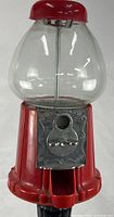 Close view of upper dispenser showing red plastic body, clear globe, coin mechanism