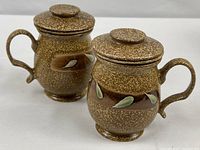 Two matching ceramic tea mugs with lids displayed side by side
