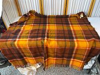 Full view of multicolor plaid wool blanket draped to show size, pattern, fringe