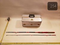 Closed aluminum tackle box, two-piece rod laid out for scale